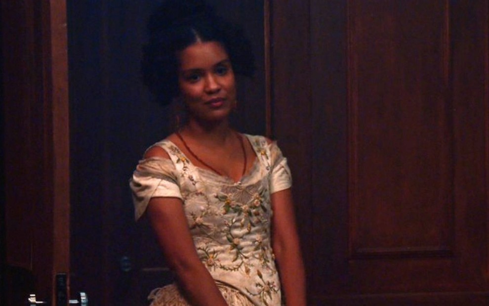 Zayla (Heslaine Vieira) está parada próxima à porta no gabinete de Tonico (Alexandre Nero) em cena de Nos Tempos do Imperador