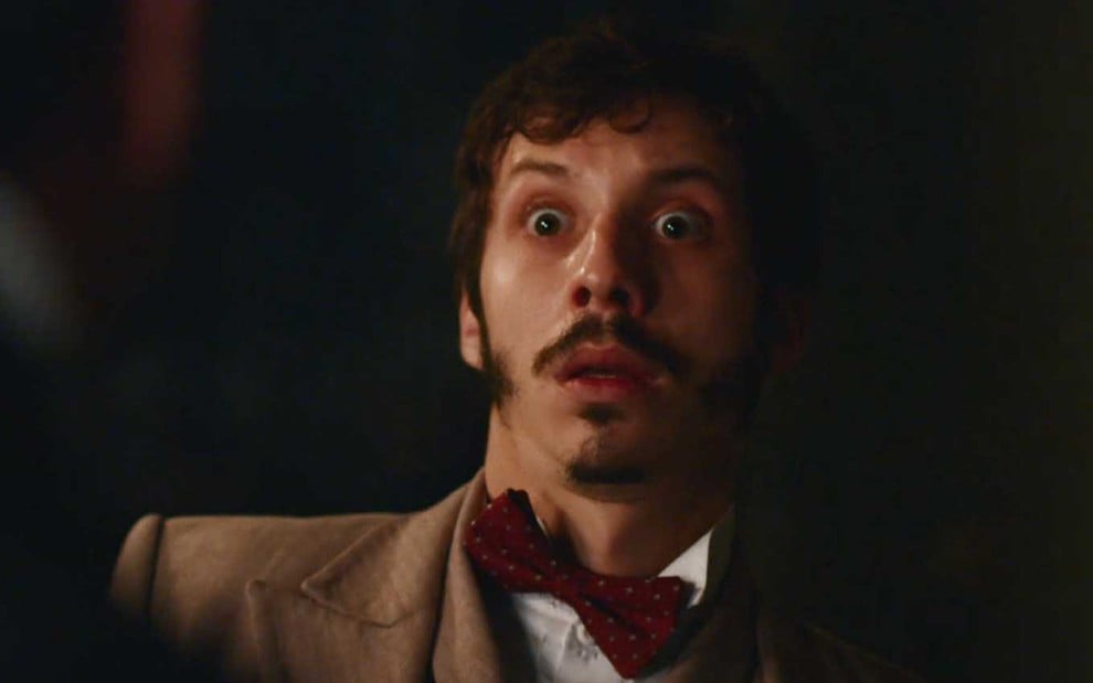 O ator João Pedro Zappa com os olhos arregalados como Nélio em cena noturna de Nos Tempos do Imperador