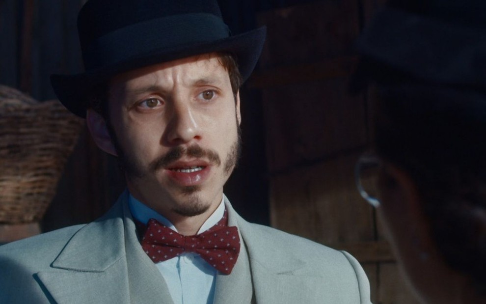 Nélio (João Pedro Zappa) usa chapéu e está sem óculos em cena de Nos Tempos do Imperador