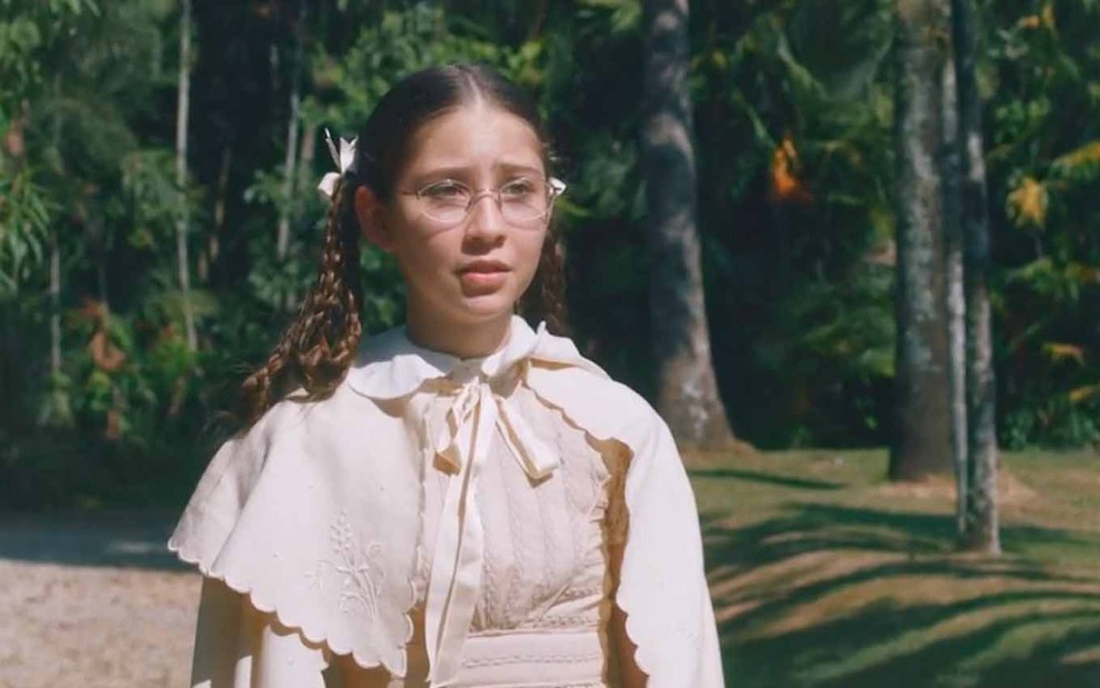 A atriz Júlia Freitas está no jardim de um palácio com expressão de desespero como a Dolores em cena de Nos Tempos do Imperador