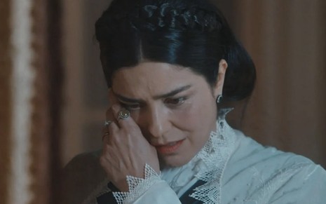 A atriz Leticia Sabatella caracterizada como Teresa Cristina limpa as lágrimas do rosto com a mão direita em cena de Nos Tempos do Imperador