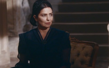 Teresa Cristina (Leticia Sabatella) está sentada em uma poltrona na sala da Quinta da Boa Vista em cena de Nos Tempos do Imperador