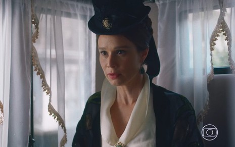 Mariana Ximenes grava com chapéu preto, cabelo preso e expressão assustada como Luísa de Nos Tempos do Imperador