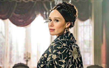 A atriz Mariana Ximenes está de perfil, com um xale preto com flores brancas bordadas, como a Luísa em cena de Nos Tempos do Imperador