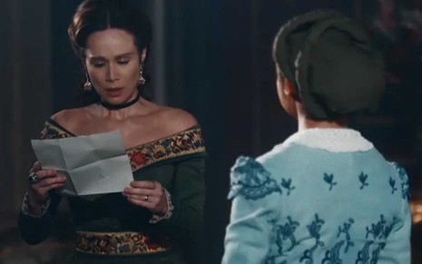 A atriz Mariana Ximenes como Luísa lê uma carta com expressão de apreensão como a Luísa em cena de Nos Tempos do Imperador