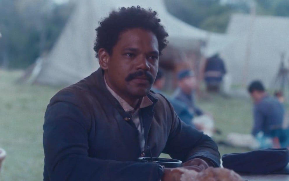 O ator Michel Gomes, de farda, em um acampamento militar como o Samuel em cena externa e diurna de Nos Tempos do Imperador