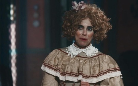 A atriz Paula Cohen, com um figurino, maquiagem e uma peruca completamente exagerados, que lembram um palhaço, como a Lota em cena de Nos Tempos do Imperador