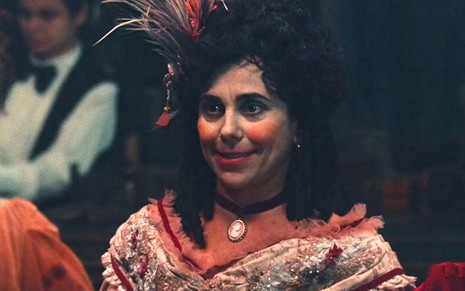 Lota (Paula Cohen) está em pé no cassino em cena de Nos Tempos do Imperador