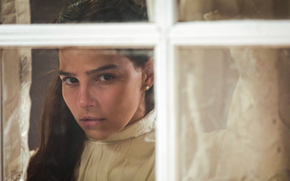 Gabriela Medvedovski em cena de Nos Tempos do Imperador: caracterizada como Pilar, atriz olha através de uma janela