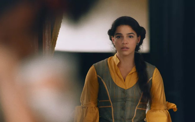 Gabriela Medvedovski grava com cabelo preso, vestido cinza e amarelo e expressão de decepção como Pilar de Nos Tempos do Imperador