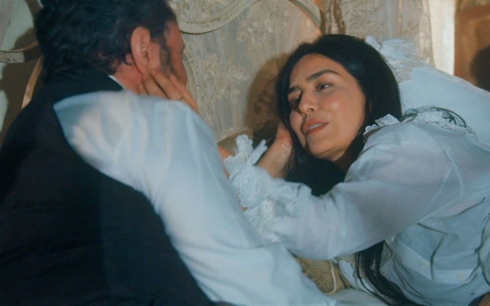 Toda feliz, Letícia Sabatella, caracterizada como Teresa Cristina, acaricia o rosto de Selton Mello, o dom Pedro 2º, em cena Nos Tempos do Imperador. Os dois estão deitados em uma cama, com vestes de dormir.