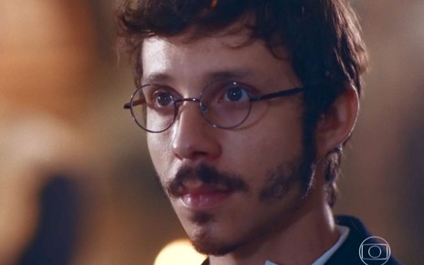 João Pedro Zappa em cena de Nos Tempos do Imperador: caracterizado como Nélio, ator está em close e olha com atenção alguém fora do quadro
