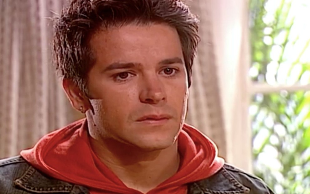 Murilo Benício em cena de O Clone: ator está com jaqueta jeans e blusa de capuz vermelho