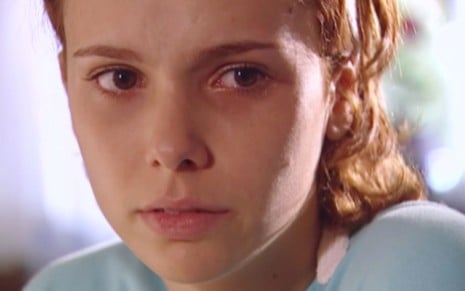 Débora Falabella em cena de O Clone: atriz usa regata azul clara, está sentada e olha confusa para o lado direito
