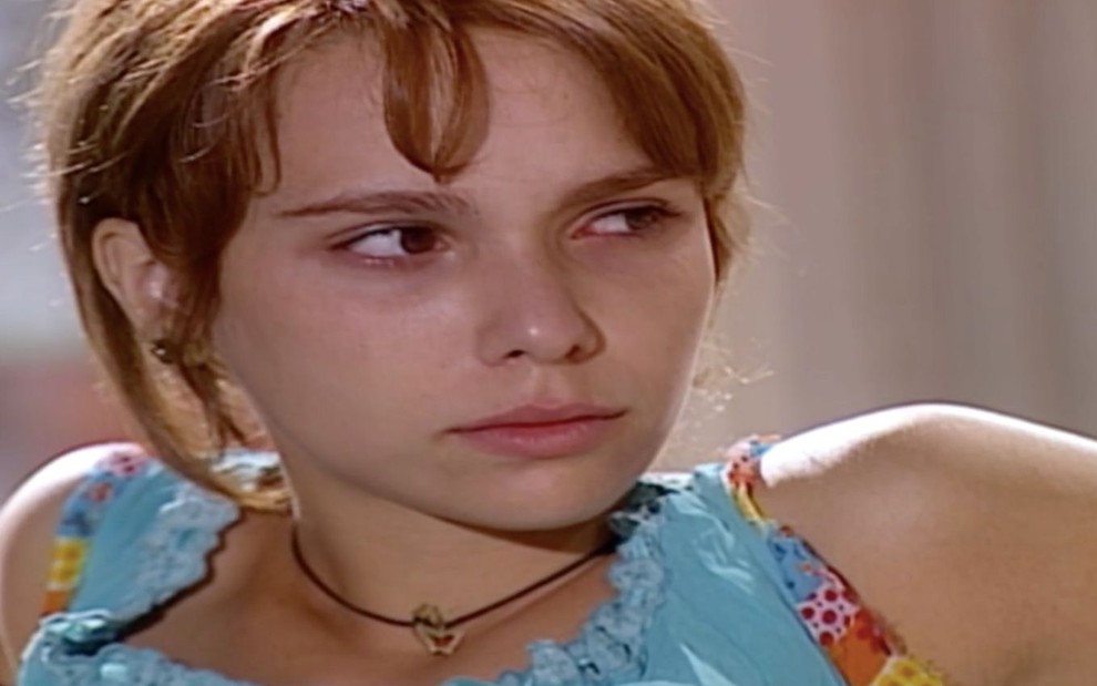 Débora Falabella em cena de O Clone: atriz usa regata azul clara, está sentada e olha confusa para o lado direito