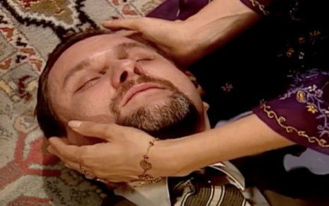 Antonio Calloni em cena de O Clone: ator está deitado no chão e é amparado por mãos femininas