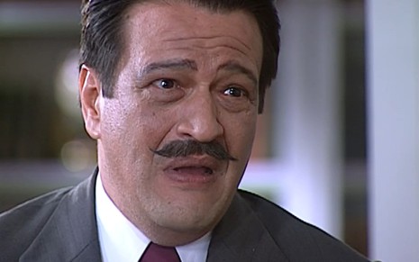 Luís Melo, caracterizada como Batista, tem a expressão angustiada, com a boca aberta e a testa franzida, em cena de O Cravo e a Rosa