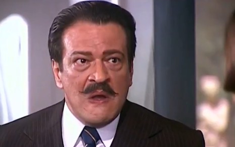 Luís Melo, caracterizado como Batista, encara ponto fixo com semblante chocado em cena de O Cravo e a Rosa