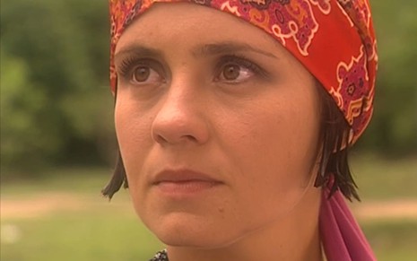 Adriana Esteves usa um lenço vermelho sobre o cabelo curto; a expressão da atriz está concentrada em cena de O Cravo e a Rosa