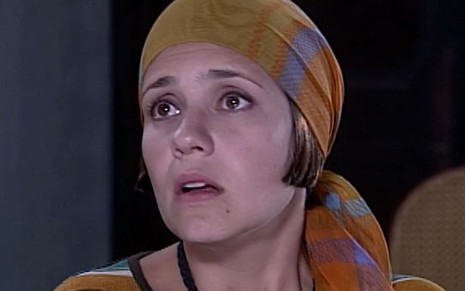 Adriana Esteves, caracterizada como Catarina, olha para além da câmera, desesperada; ela usa um lenço na cabeça em cena de O Cravo e a Rosa