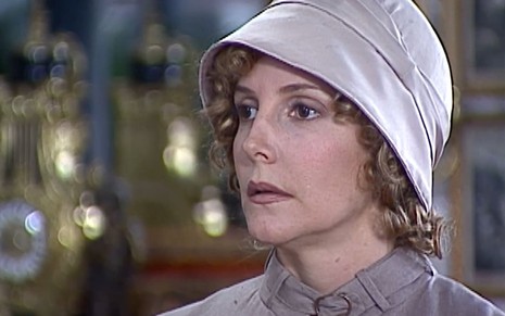 Maria Padilha, caracterizada como Dinorá, tem o semblante preocupado em cena de O Cravo e a Rosa; ela usa um chapéu e um vestido rosados