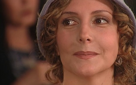 Maria Padilha tem os cabelos na altura do queixo, cobertos com um chapéu cinza, e olha para o lado em cena de O Cravo e a Rosa