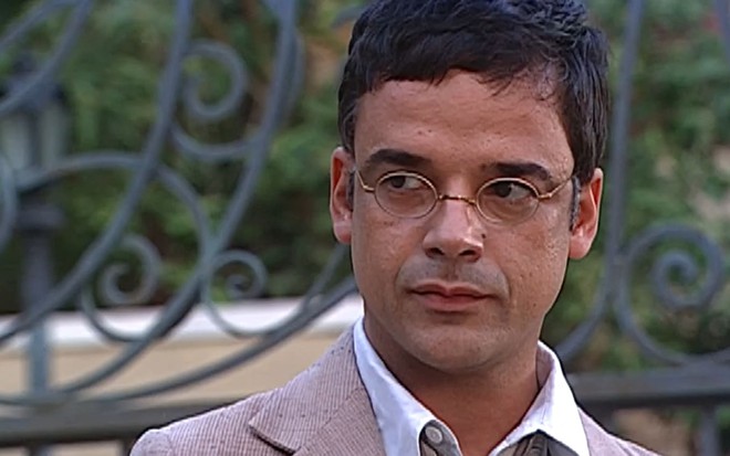 Ângelo Antônio tem o semblante emburrado em cena de O Cravo e a Rosa; ator usa um paletó gasto e um óculos pequeno