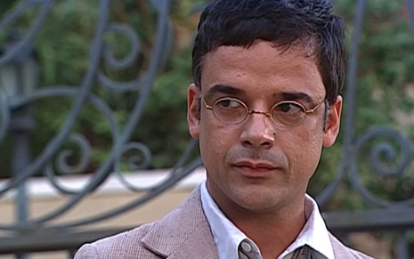 Ângelo Antônio tem o semblante emburrado em cena de O Cravo e a Rosa; ator usa um paletó gasto e um óculos pequeno