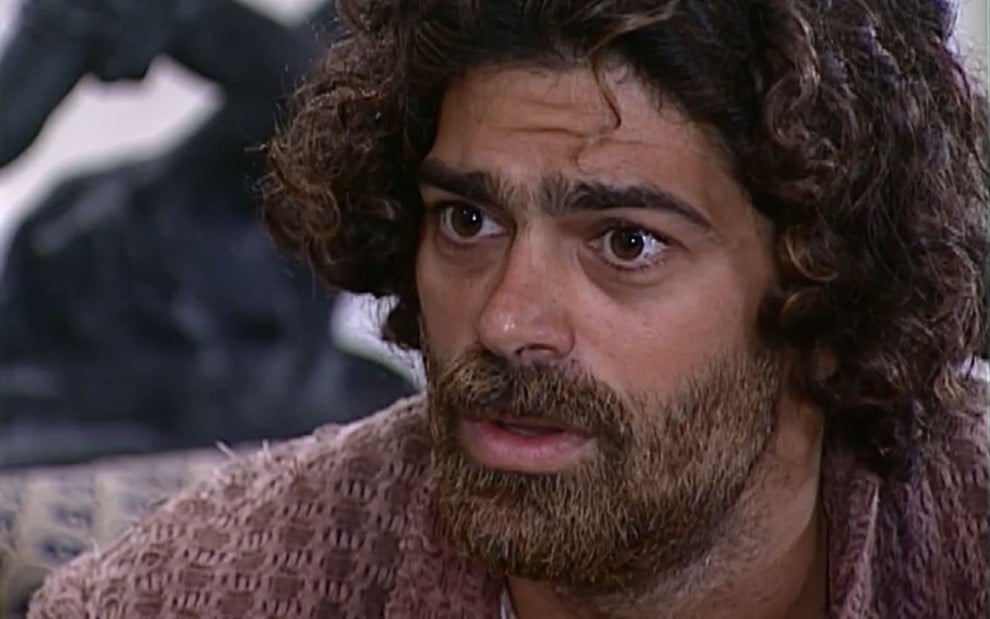 Eduardo Moscovis caracterizado como Petruchio: ele está cabelo e barba longos, sobrancelha por fazer e blusa surrada em cena de O Cravo e a Rosa.