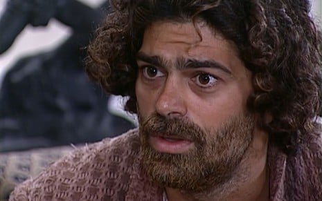 Eduardo Moscovis caracterizado como Petruchio: ele está cabelo e barba longos, sobrancelha por fazer e blusa surrada em cena de O Cravo e a Rosa.