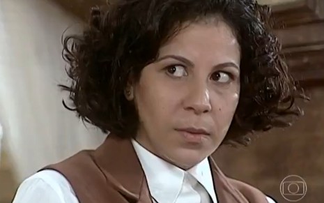 Carla Daniel, caracterizada como Lourdes, espia Carlos Evelyn, o Fábio, de rabo de olho em cena de O Cravo e a Rosa