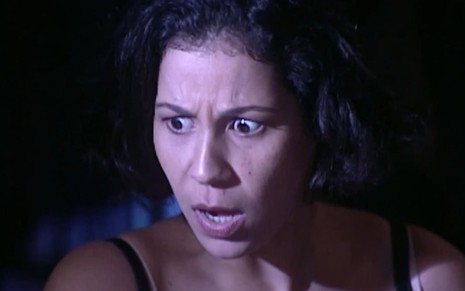 Carla Daniel, caracterizada como Lourdes, está boquiaberta em cena de O Cravo e a Rosa