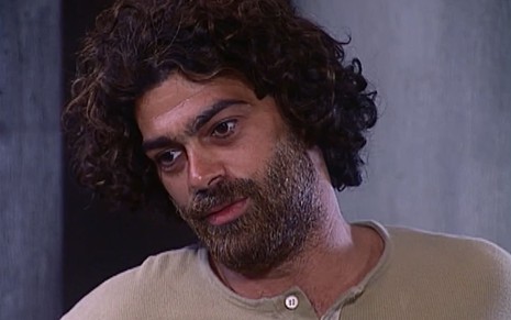 Eduardo Moscovis caracterizado como Petruchio: cabelo e barba longos, sobrancelha por fazer e blusa surrada. Ele tem a feição abatida em cena de O Cravo e a Rosa.