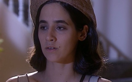 Marina Lima caracterizada como Liliana; ela tem os cabelos pretos na altura dos ombros e veste uma blusa branca em cena de O Rei do Gado