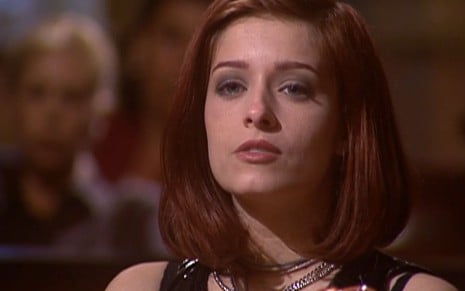 Luciana Vendramini caracterizada como Marita; ela tem os cabelos vermelhos curtos e exibe choque em cena de O Rei do Gado