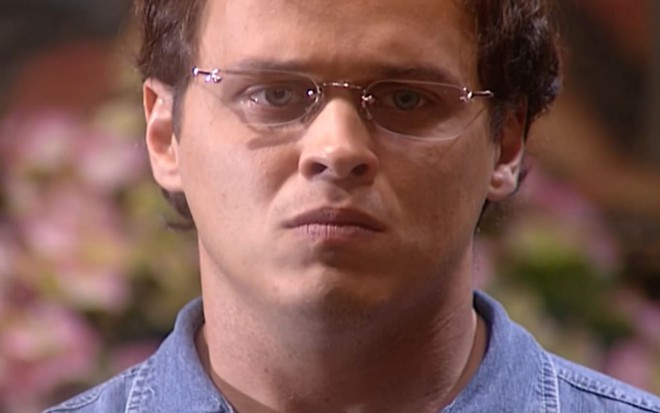 Guilherme Fontes caracterizado como Otávio; ele usa uma boina e suéter surrados e tem o semblante sério em cena de O Rei do Gado