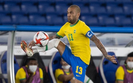 Com uniforme tradicional da Seleção Brasileira, Daniel Alves dá um salto para dominar a bola em jogo de futebol