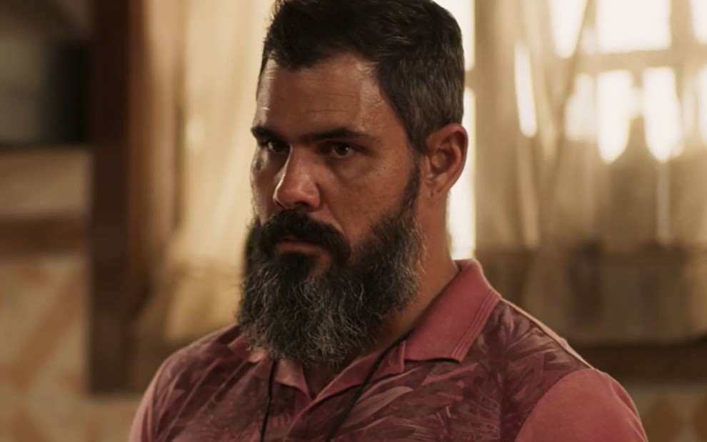 Juliano Cazarré tem o cabelo curto e a barba longa; o ator tem a expressão raivosa --as sobrancelhas franzidas, a boca apertada-- em cena de Pantanal
