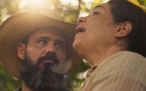 Juliano Cazarré, caracterizado como Alcides, encara Isabel Teixeira, a Maria Bruaca, com um olhar apaixonado em cena de Pantanal; ao fundo, é possível ver o pôr-do-sol