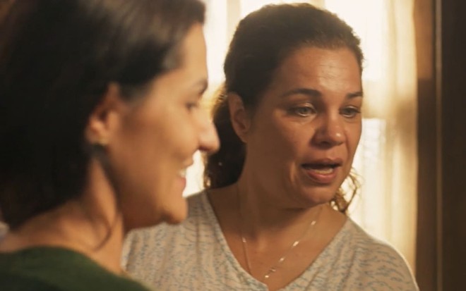 Paula Barbosa, caracterizada como Zefa, está de perfil para a câmera, sorrindo; Isabel Teixeira, a Maria Bruaca, está boquiaberta em cena de Pantanal