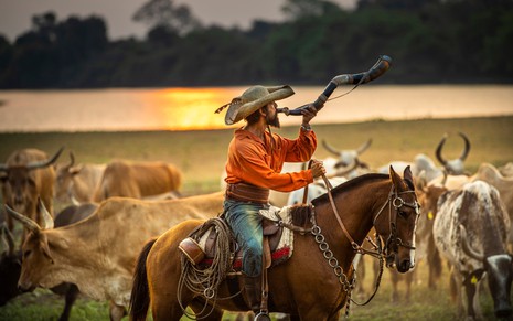 Montado em cavalo, Irandhir Santos, caracterizado como Joventino, toca o berrante em cena de Pantanal