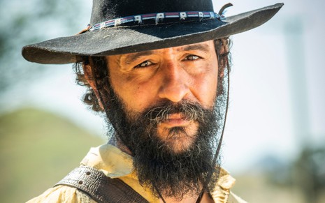 Irandhir Santos, caracterizado como Joventino: barba e bigode longos e rosto com marcas de sol. Ele usa um chapéu de couro e tem o semblante sério em ensaio fotográfico de Pantanal.