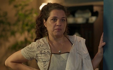 Isabel Teixeira, caracterizada como Maria Bruaca, exibe rosto sem maquiagem e cabelos amarrados; ela tem o semblante sério enquanto se apoia no batente da porta em cena de Pantanal