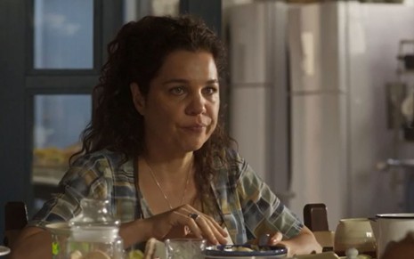 Maria Bruaca (Isabel Teixeira) está sentada à mesa em cena de Pantanal, novela das nove da Globo