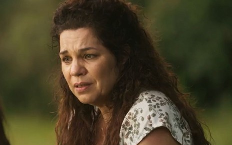 Maria Bruaca (Isabel Teixeira) está sentada em meio ao verde e tem expressão de surpresa em cena de Pantanal, novela das nove da Globo