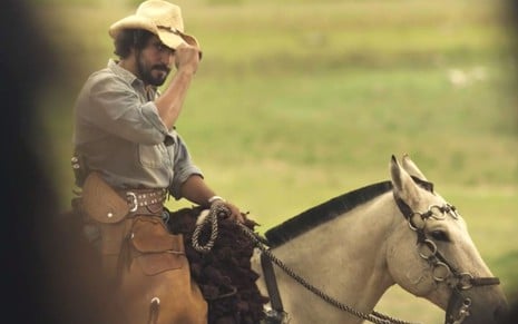 Renato Góes em cena de Pantanal: ator usa chapéu de boiadeiro, está sentado em cavalo e olha para alguém fora do quadro