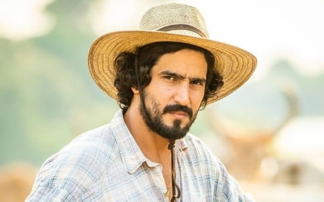 Renato Góes está caracterizado como o peão José Leôncio de Pantanal, novela das nove da Globo; ele usa chapéu e camisa xadrez