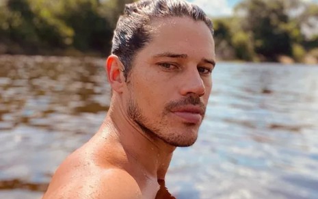 José Loreto tem os cabelos molhados e jogados para trás; ele está imerso no rio, sem camisa e apenas com o rosto para fora das águas