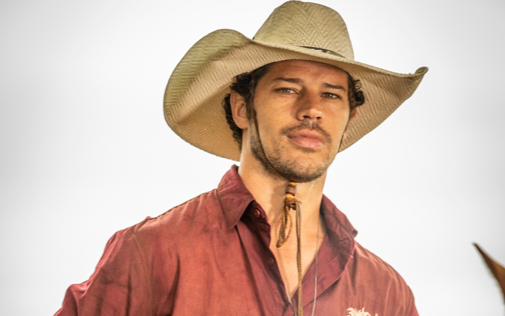 José Loreto, caracterizado como Tadeu: ator usa chapéu de palha e veste camisa vermelha em ensaio fotográfico de Pantanal