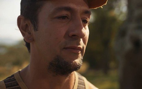 Irandhir Santos caracterizado como José Lucas: ele usa cavanhaque e veste uma regata listrada. O cabelo cacheado está coberto por um boné preto em cena de Pantanal